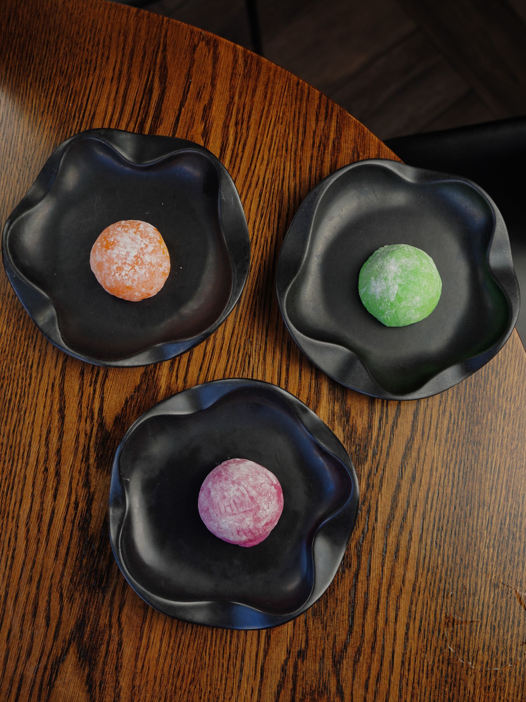 Tres mochis de colores sobre platos negros con forma de flor